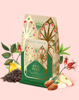 A decorative bag of Apple Almond Nog—a mood-boosting black tea and delightful eggnog alternative—is surrounded by tea leaves, apple slices, almonds, pineapple, and rose hips on a light pink background.