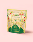 A yellow and green resealable pouch labeled “Apple Almond Nog” displays a festive, ornate design with peacock-like patterns on a pale pink background—an eggnog alternative tea that’s mood-boosting and delicious.