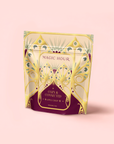 A decorative stand-up pouch with a pale yellow and purple design labeled "Magic Hour" and "Apple Crisp Oolong: Cozy & Connected," featuring this autumn tea blend against a light pink background.