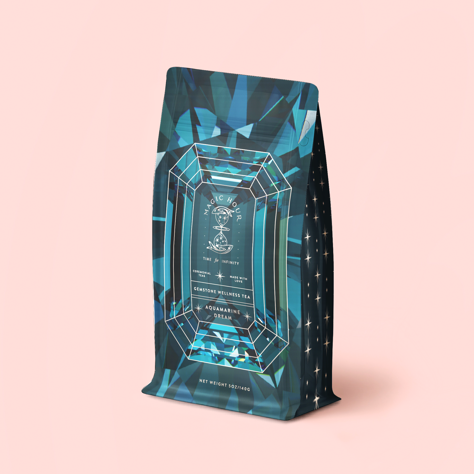 A blue geometric tea bag package labeled "Aquamarine Dream - Soothing Herbal Ayurvedic Adrenal Tonic Refill Pouch" sits upright on a pale pink background, adorned with star patterns and gemstone-inspired designs. This aquamarine blend is a calming herbal infusion designed to soothe the senses and promote peaceful evenings.