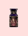 A decorative bottle of Magic Hour tea labeled "Artemis of the Wilds: Wild Moon White Tea," featuring an ornate design with a celestial figure and floral patterns on a light pink background, contains wild moon white tea for a delicate, low-caffeine tea experience.