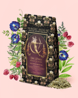 A floral-decorated tea package labeled "Monthly Magic Tea Journey Subscription," surrounded by illustrated flowers, raspberries, and loose tea leaves, invites you to a ceremonial journey with goddess tea on a pastel pink background.