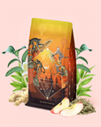 A vibrant Bali Bliss: Coconut-Lime & Ginger-Melon White Tea package featuring jungle animals, a figure, and a golden sunset design, surrounded by ginger, apple slices, green leaves, and botanical elements on a light pink background. This captivating display perfectly captures the essence of this tropical white tea blend and highlights its refreshing anti-inflammatory allure.