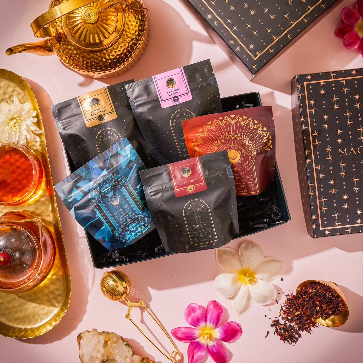 Bestsellers of Magic Tea Starter Set- 60-75 cup sampler box featuring four pouches arranged next to a gold teapot, a tea strainer, and loose-leaf tea.
