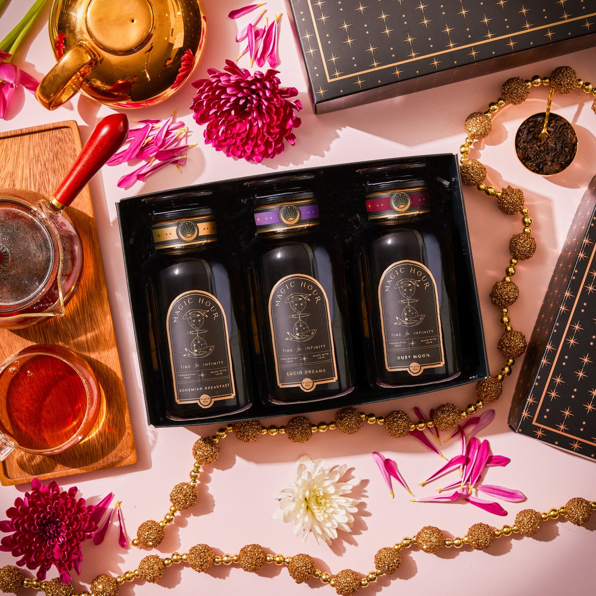 Best Sellers of Magic Hour Trio Box featuring three organic tea blends—Bohemian Breakfast, Lucid Dreams, and Ruby Moon—in a black gift box, surrounded by a teapot, a cup of tea, and floral accents.