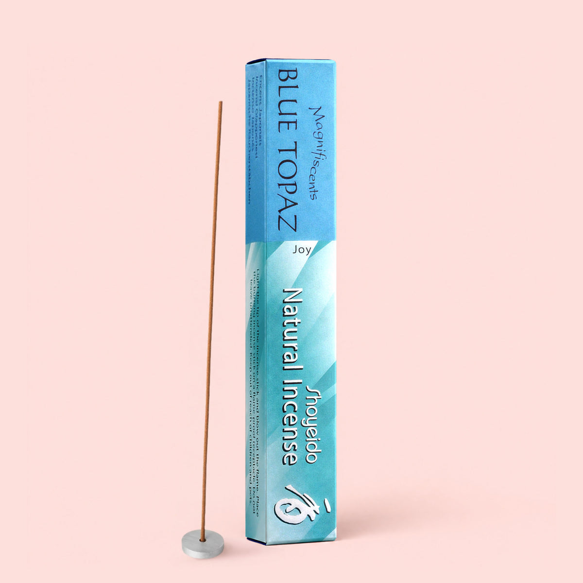 A box of Blue Topaz Natural Incense stands upright next to a single vanilla incense stick placed in a small round holder, set against a light pink background.