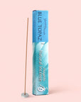 A box of Blue Topaz Natural Incense stands upright next to a single vanilla incense stick placed in a small round holder, set against a light pink background.