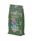 A green, floral-themed bag of Blueberry Lavender Mint: Cosmic Garden Iced Tea by Magic Hour. The packaging features illustrations of blueberries, lavender, butterflies, and stars, with the flavors listed as blackberry, lavender, and mint. Enjoy this delightful loose leaf tea blend for an organic tea experience.