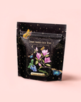 A black resealable pouch labeled "Blueberry Cheesecake Oolong Iced Tea" features magnolia flowers, butterflies, and stars on a light pink background, highlighting its premium organic oolong tea blend.