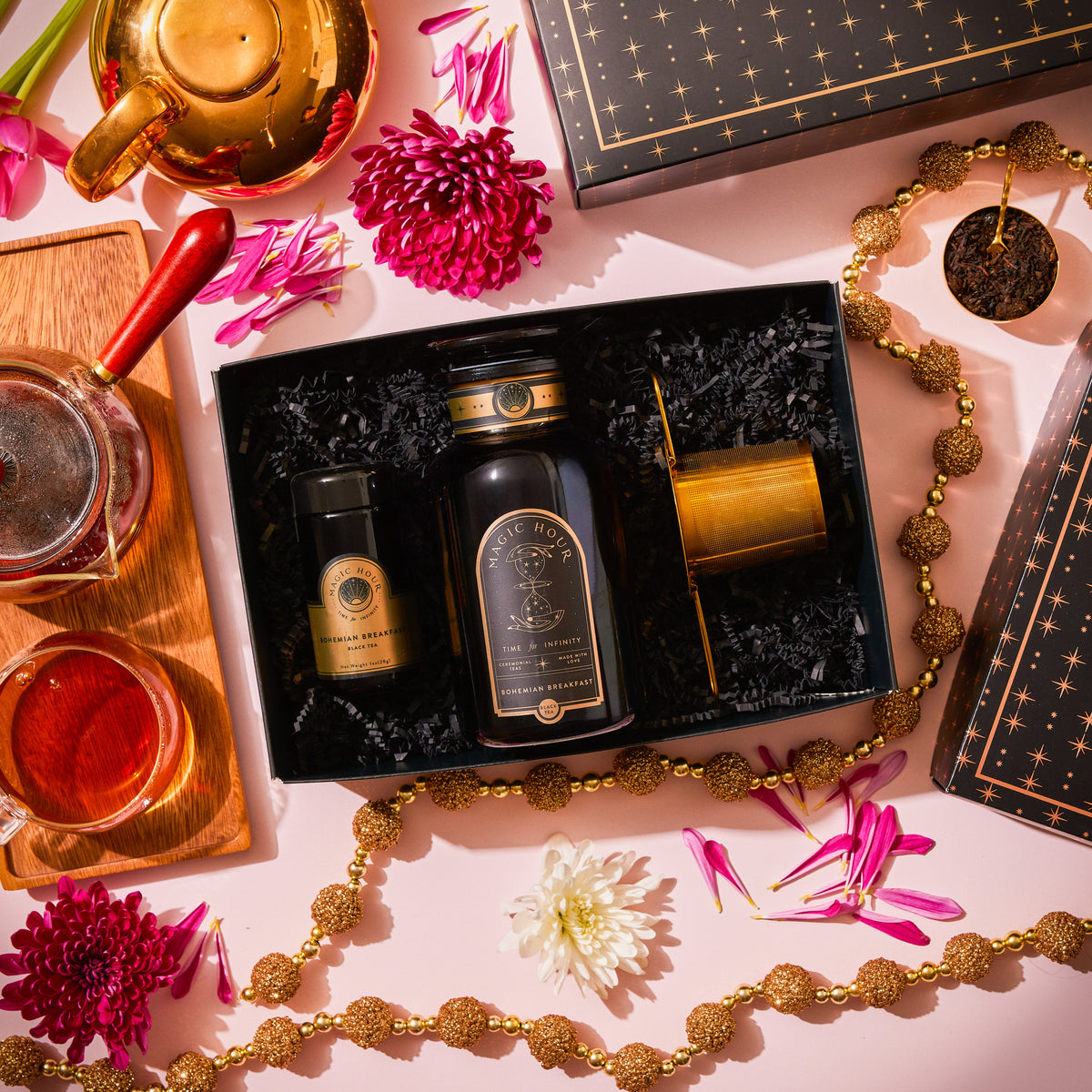 The Bohemian Breakfast Apothecary & Traveler Set with Midas Touch features a large glass tea jar, a small tea tin, and a strainer, arranged with a teapot, a cup of tea, and floral accents.