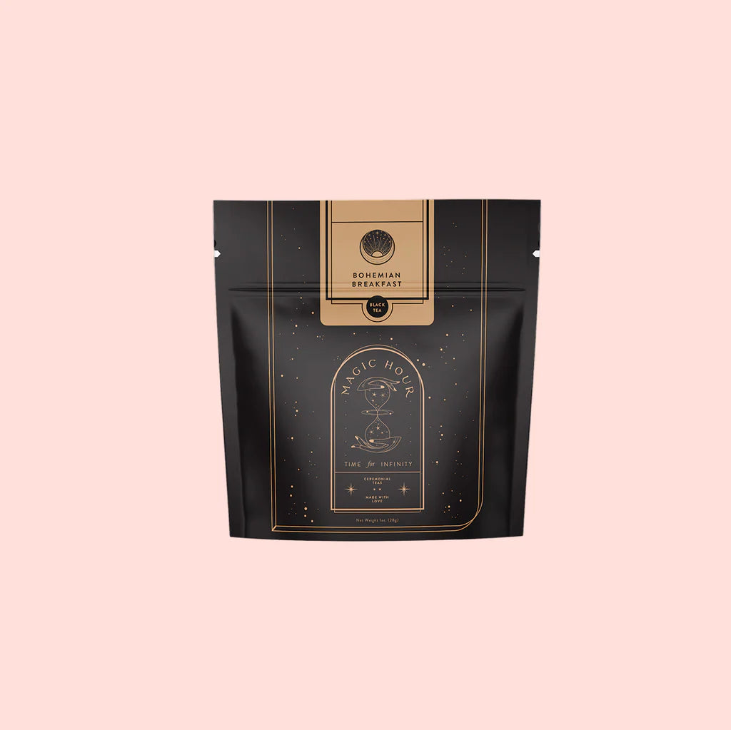 A black and gold resealable pouch labeled “Bohemian Breakfast Black Tea—Probiotic Rich Vanilla Puerh Tea for Digestion &amp; Energy,” with celestial designs, sits against a light pink background.