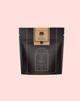 A black and gold resealable pouch labeled “Bohemian Breakfast Black Tea—Probiotic Rich Vanilla Puerh Tea for Digestion & Energy,” with celestial designs, sits against a light pink background.