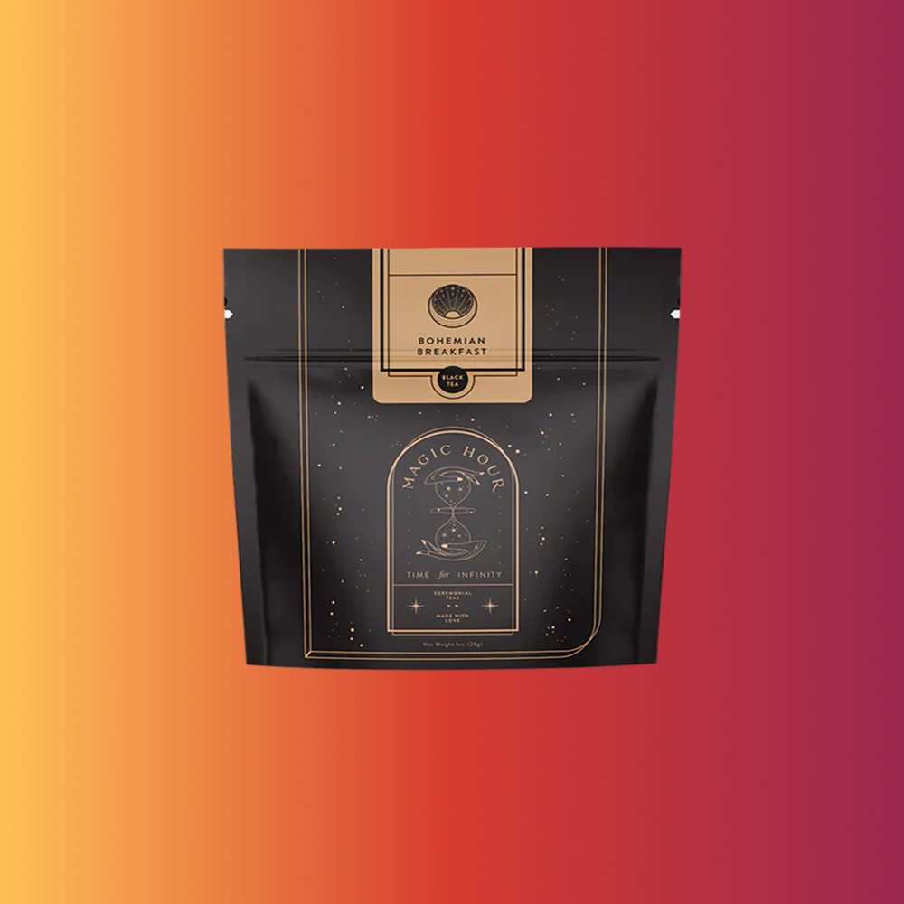 A black and gold resealable pouch labeled "Bohemian Breakfast Black Tea- Probiotic Rich Vanilla Puerh Tea for Digestion & Energy" by Magic Hour, with a celestial design, highlights this organic coffee alternative against a light pink background.