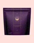 A purple resealable tea package with gold star patterns and a "Magic Hour" gold logo sits on a light pink background. The packaging features Aquarius: Visionary Goddess Tea, an Organic Golden Monkey Tip Black Tea from Yunnan gardens.