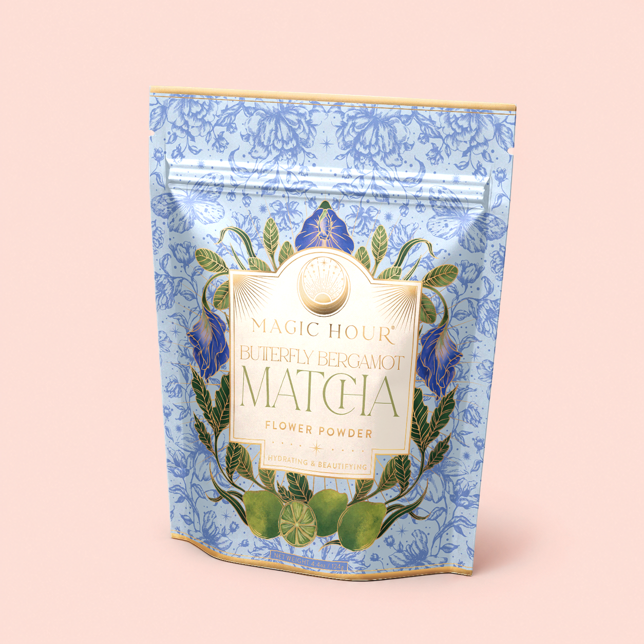 A blue floral-patterned pouch labeled “Flower Powder: Butterfly Bergamot Matcha”—featuring a blend of ceremonial matcha and butterfly pea flower—rests amid green leaves and limes on a pale pink background.