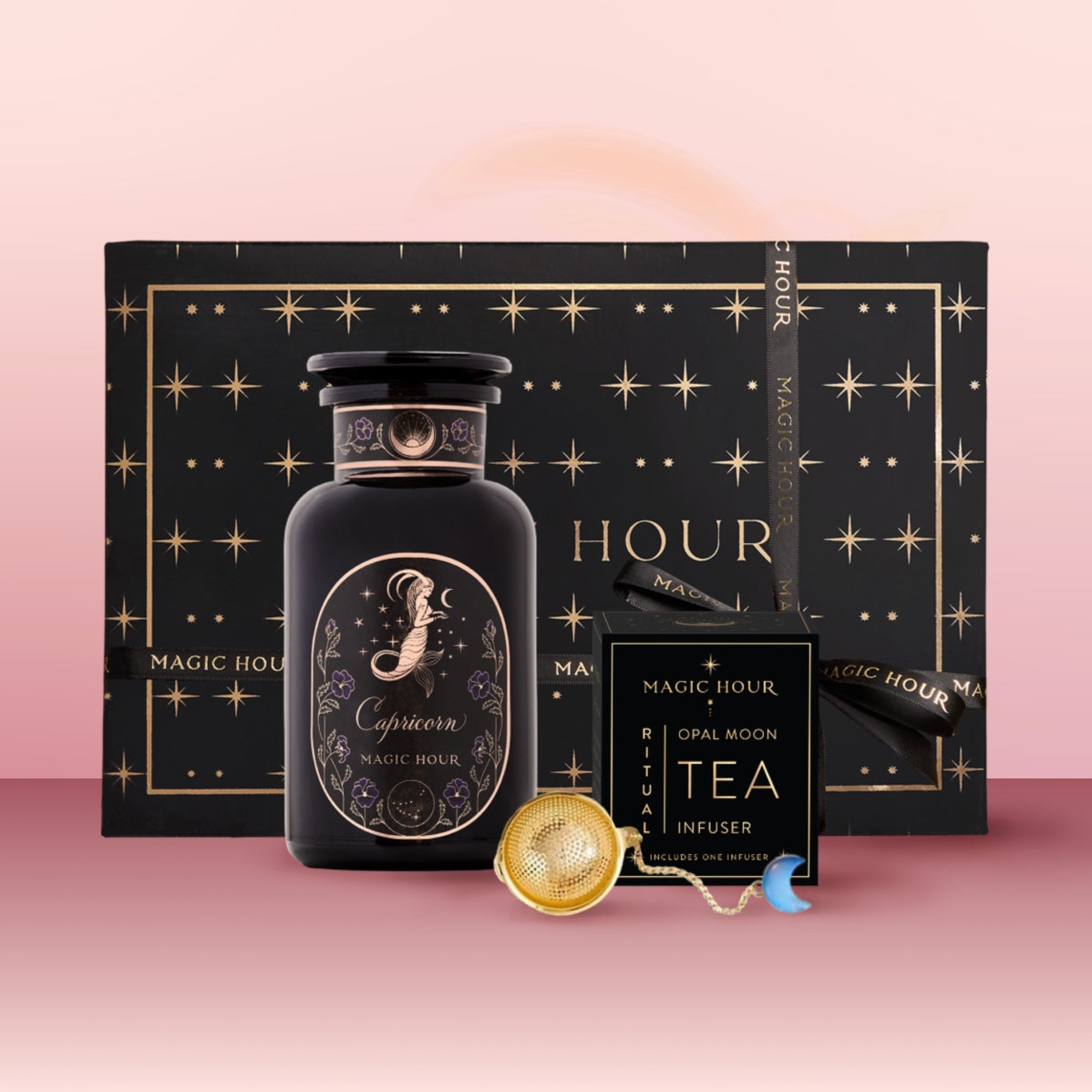 A black starry "Magic Hour" gift box holds the Capricorn Astrology Tea Gift Set, including a Capricorn tea jar, Opal Moon Ritual Tea, and an Opalite Moon Tea Strainer, set on a pink gradient background.