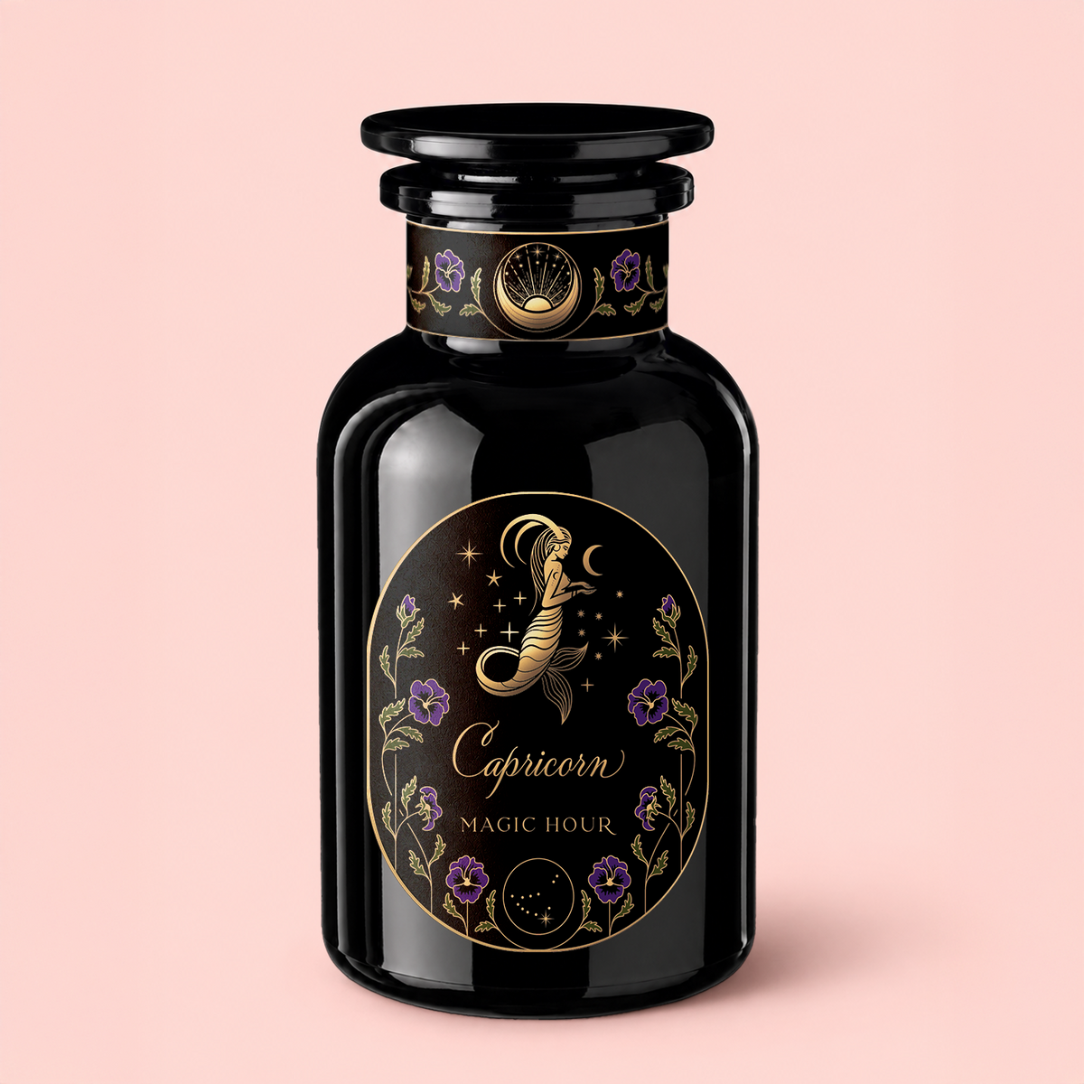 A black glass bottle labeled “Capricorn: Maple Oolong Tea” features a gold and purple zodiac-themed Capricorn design with floral details and “Magic Hour” text, emphasizing the metabolism-boosting benefits of Ti Quan Yin Oolong and Se Chung Oolong, all set against a soft pink background.