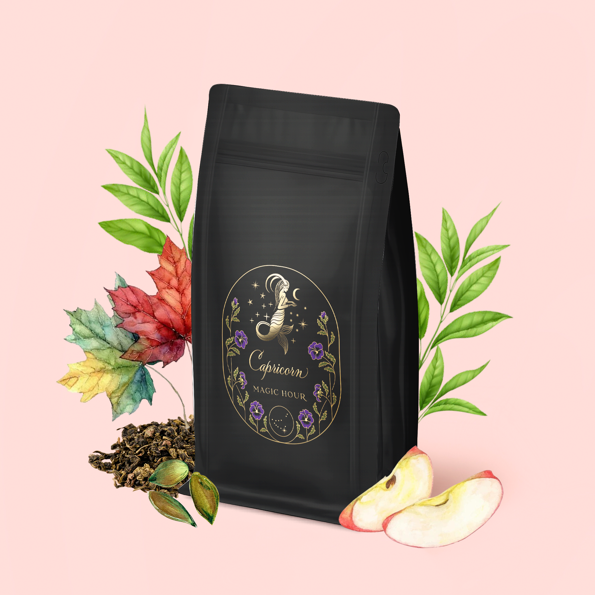A bag of Capricorn: Maple Oolong Tea with a gold and purple Capricorn label stands on a pink background, surrounded by green leaves, apple slices, loose tea, metabolism-boosting cardamom pods, and autumn leaves.