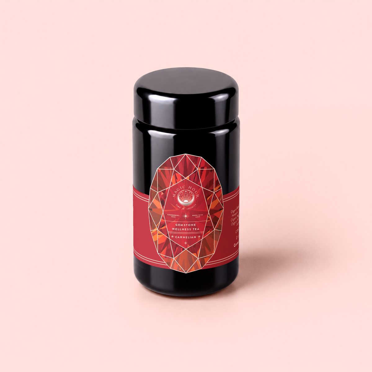 A black tea canister with a red geometric label sits on a light pink background. The label reads “Carnelian : Caffeine-Free Apricot Amaretto Tea” in white text, evoking the allure of an herbal potion.