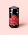 A black tea canister with a red geometric label sits on a light pink background. The label reads “Carnelian : Caffeine-Free Apricot Amaretto Tea” in white text, evoking the allure of an herbal potion.
