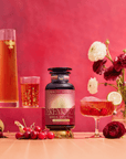 A bottle of Cherry Cola Black Tea: Ceremonial Soda Pop Tea with Sugar "Destroyer" sits among glasses of tea, cherries, sliced lime, loose tea leaves, and red and white flowers on a vibrant red background.