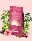 A pink bag of Cherry Cola Black Tea: Ceremonial Soda Pop Tea—a delicious cherry cola–flavored tea made with a natural sweetener—rests surrounded by hibiscus, cherries, cinnamon sticks, and green leaves on a pastel pink background.
