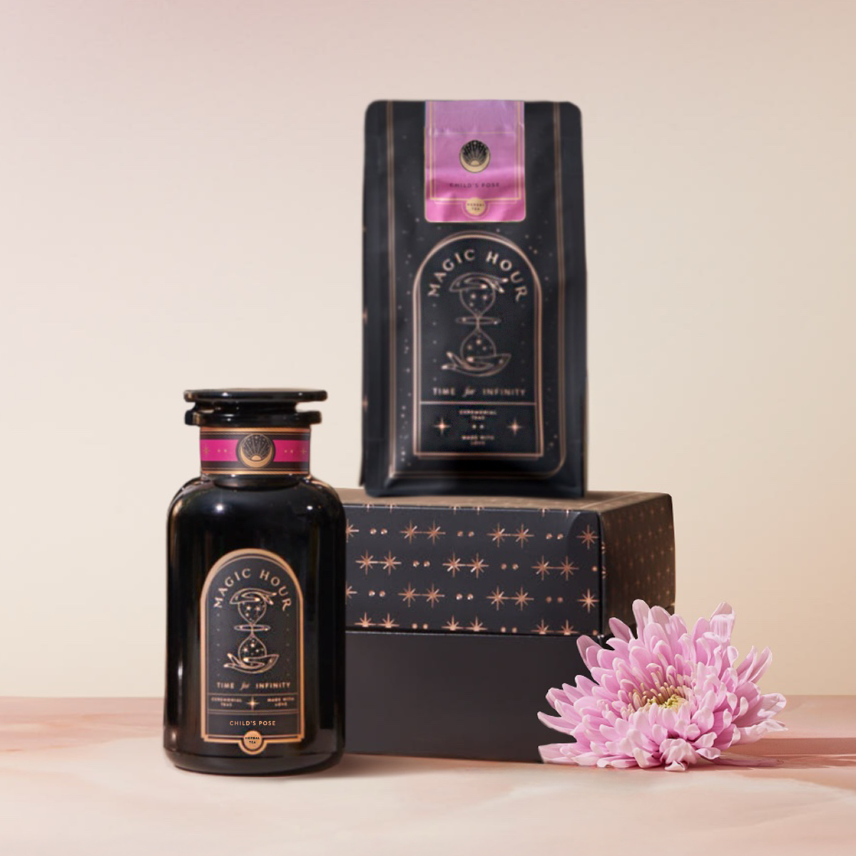 A dark glass jar and matching coffee bag labeled "Child’s Pose™ Starter Kit: Herbal Adaptogen Tea Blend for Sleep & Restful Calm" rest on a star-patterned box, inviting you to unwind with calming tea. A light purple chrysanthemum accents the pale pink scene.