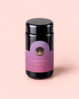 A canister of Child’s Pose™ Herbal Adaptogen Tea for Sleep Case Packs, featuring purple and gold accents, rests on a soft pink background and highlights its organic ingredients designed to provide soothing, aromatherapeutic benefits.
