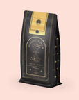 A black and gold bag labeled "Citrine Cleanse™ Herbal Tea" features an hourglass design with celestial motifs. It includes "Ceremonial" and "120g / 4.2oz" on a soft pink background, reminiscent of a detoxifying elixir infused with organic ingredients.