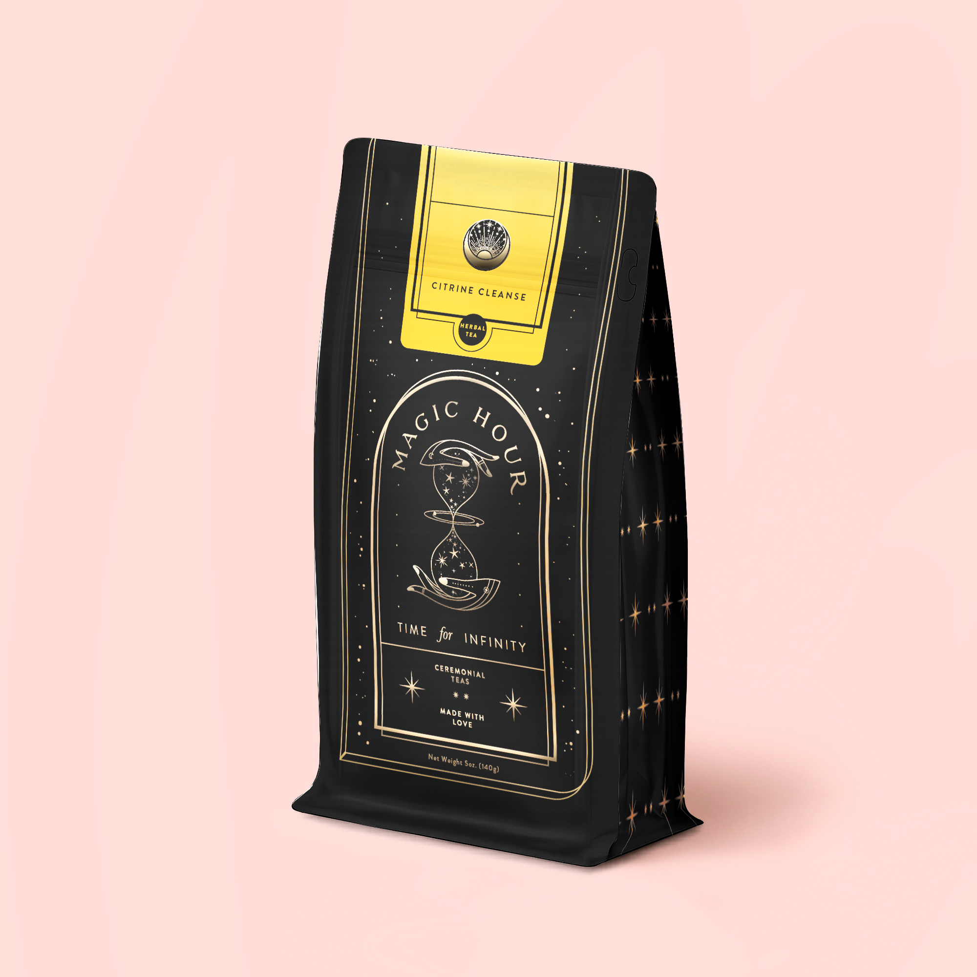 A black and gold "Magic Hour" tea bag with an hourglass, stars, and a yellow "Citrine Cleanse" label contains Citrene Cleanse™ Herbal Tea Refill Pouch, a caffeine-free blend with organic Hawaiian Ginger for detox. Set on pale pink.