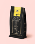 A black and gold "Magic Hour" tea bag with an hourglass, stars, and a yellow "Citrine Cleanse" label contains Citrene Cleanse™ Herbal Tea Refill Pouch, a caffeine-free blend with organic Hawaiian Ginger for detox. Set on pale pink.