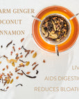 A glass teacup with a metal handle filled with a warm, amber-colored herbal tea is surrounded by scattered loose leaf tea ingredients like ginger, coconut, and cinnamon on a white surface. Text around the cup highlights benefits: "Liver," "Aids Digestion," and "Reduces Bloating. The tea is Zhena’s Original Coconut Chai from Club Magic Hour.