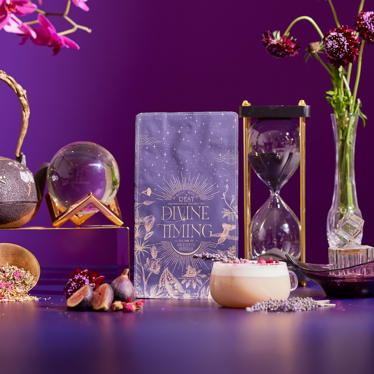 A styled scene features the "Divine Timing Rest" card deck at the center, surrounded by an hourglass, crystal ball, figs, a latte, flowers, and crystals on a purple background.