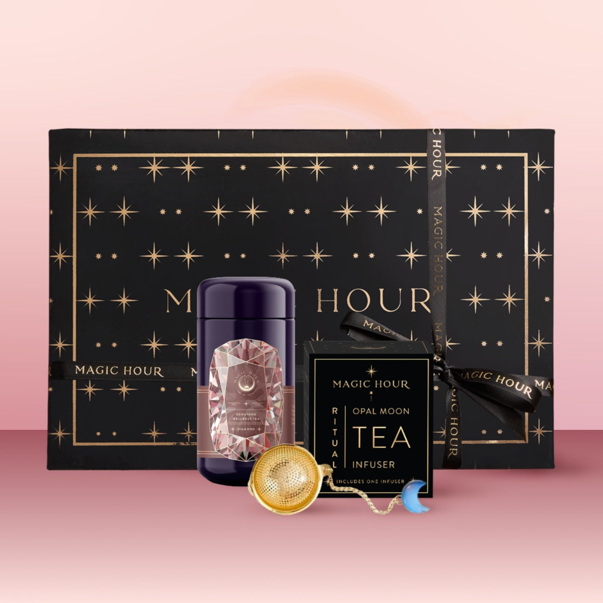A black and gold star-themed "Diamond April Birthstone Mini Gift Set" is displayed with a March Wellness Tea canister, a tea infuser, a tea sachet box, and an aquamarine blue beaded tea scoop on a pink background.