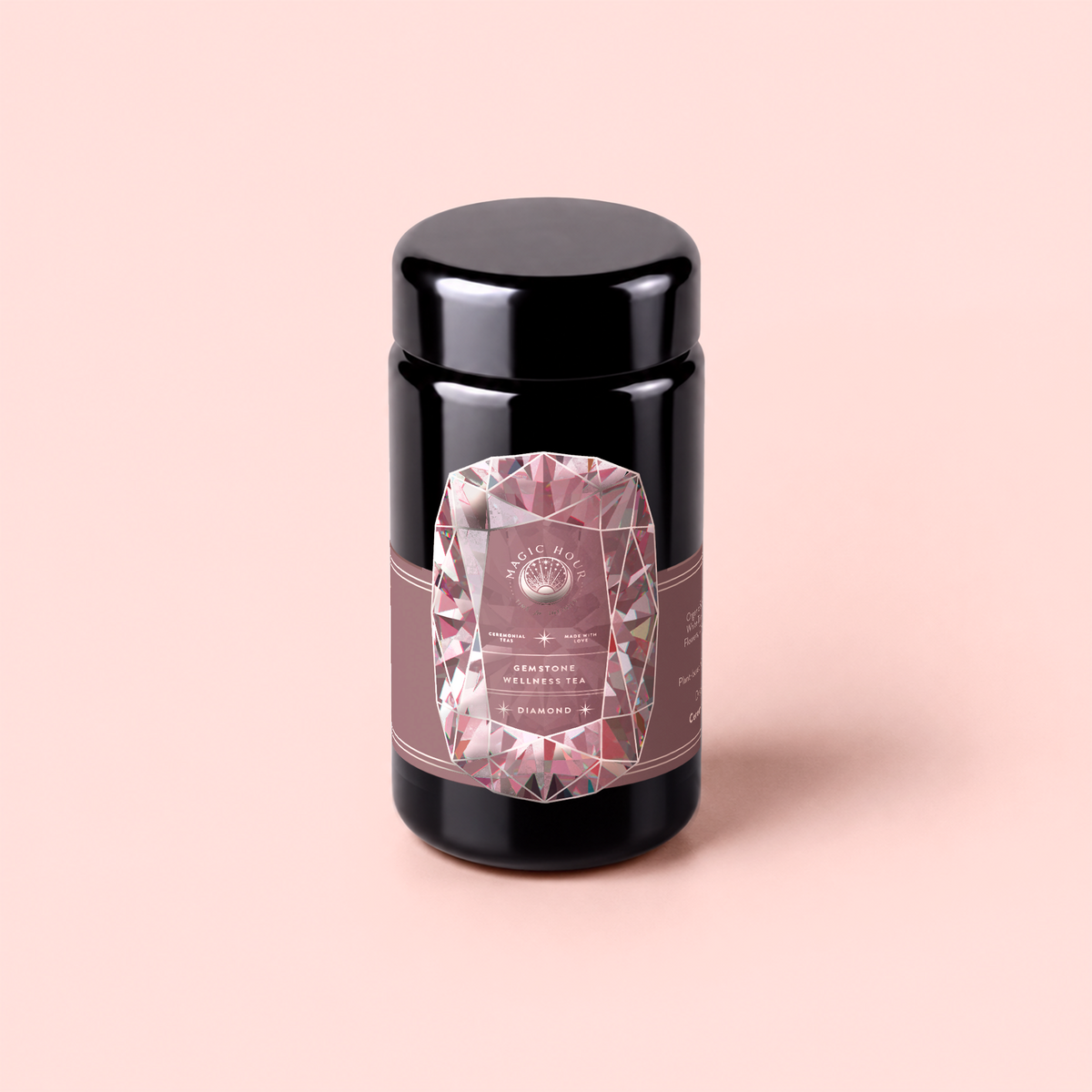 A black jar with a geometric pink and silver label stands upright on a pale pink background. The label features diamond shapes and text, highlighting “Diamond - Champagne &amp; Strawberry Jasmine White Tea for Beautiful Skin,” suggesting this is a luxurious, high-end infusion crafted to promote beautiful skin.