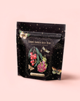A black resealable pouch features star patterns, dragonfruit and lychee botanicals, and colorful moths. The label reads "Dragonfruit Lychee Green Iced Tea" with organic sencha, from Cosmic Garden Iced Teas by Magic Hour.