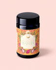 A black jar labeled "Flower Powder: Dragon Fruit Matcha" rests on a pale pink background. The label is adorned with vibrant dragon fruit illustrations and decorative patterns, emphasizing the ceremonial matcha blend crafted to support gut microbiome health.