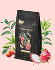 A tea bag labeled “Dragonfruit Lychee Green Iced Tea” with gold stars rests on a pale pink background, surrounded by juicy lychee, vibrant dragonfruit, and leafy branches. The infusion features organic sencha green tea for a refreshing blend.