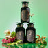 Three dark apothecary jars, labeled “Virgo,” “Capricorn,” and “Dawn,” rest among ferns, flowers, and mushrooms on a green backdrop, creating a mystical vibe—an ideal addition to the Earth Sign Astrology Bundle.
