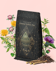 A black and gold bag of Earth: Stabilizing and Nourishing Herbs, Roots, and Puerh Tea for Digestion & Grounding stands amid illustrated herbs and roots, including dandelion, artichoke, and yellow twigs, against a soft pink background.