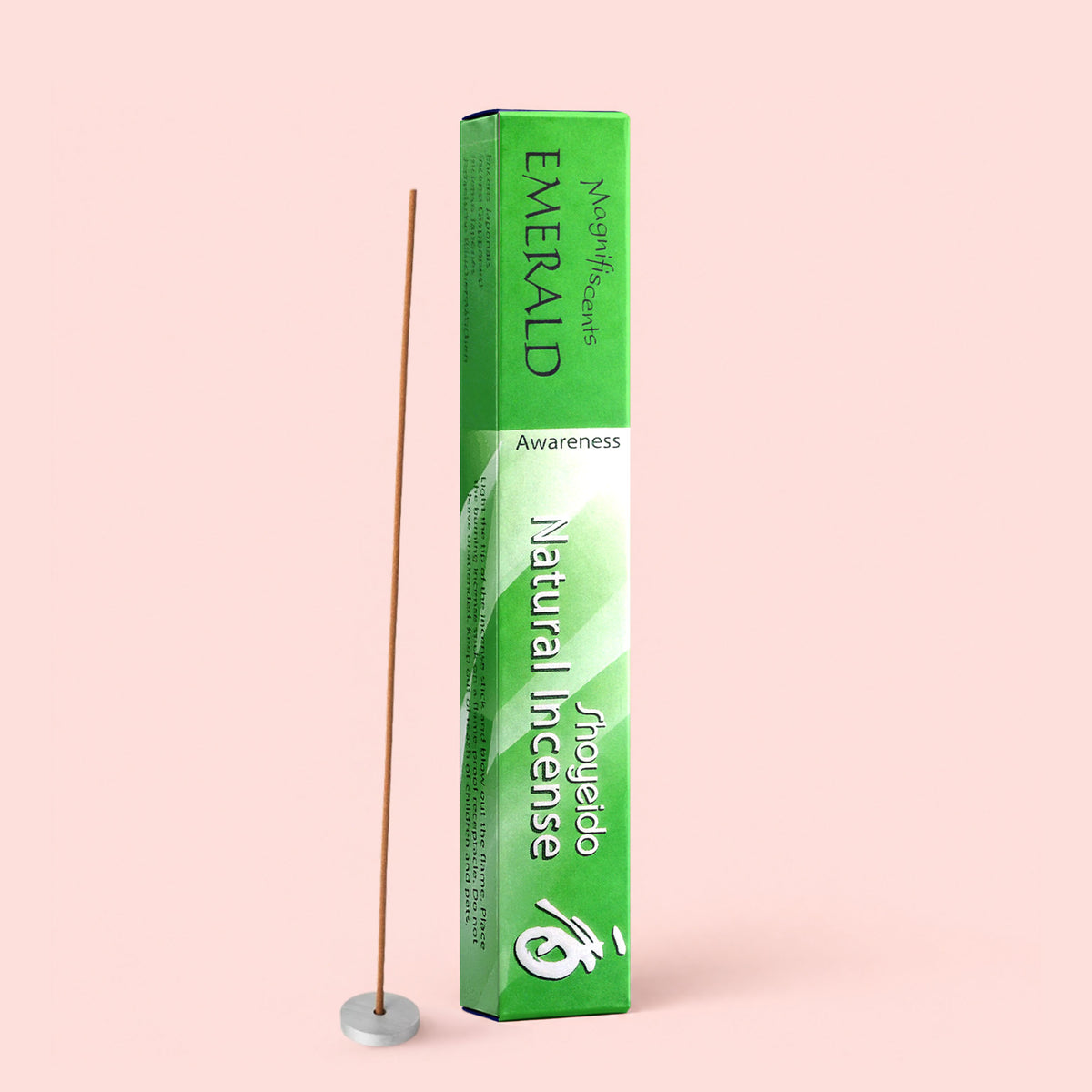 A green box labeled “Natural Incense : Emerald” stands upright next to a lit sandalwood incense stick in a small white holder, all set against a pale pink background.