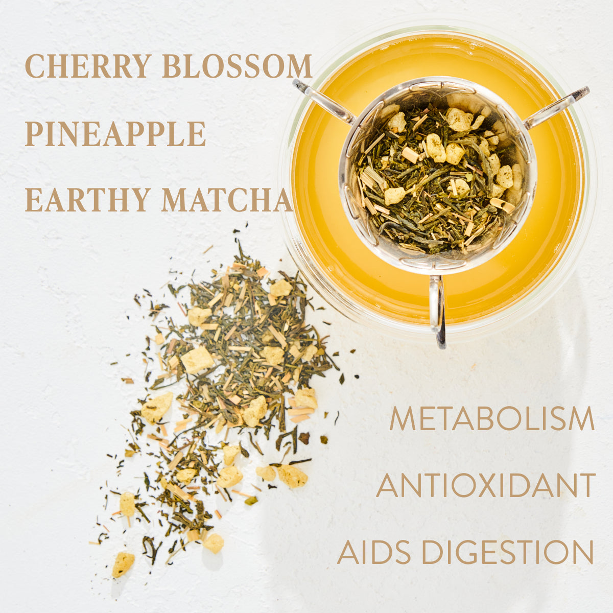 A cup of yellow tea viewed from above, with green tea leaves and pineapple pieces inside. Loose leaf tea and pineapple pieces are scattered on the table. Text on the image reads "Emerald - Cherry Blossom Pineapple Cream Green Tea, Earthy Matcha, Metabolism, Antioxidant, Aids Digestion." Experience the charm of Magic Hour.