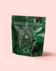 Resealable packaging for "Emerald - Cherry Blossom Pineapple Cream Green Tea" features a gemstone pattern, emerald-cut design, and circular logo on a light pink background, inspired by Japanese green tea.