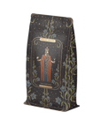 A decorated tea packaging features an illustration of a robed figure wearing a crown with "Magic Hour" at the top and "The Emperor" below. Inspired by Tarot archetypes, the background has an intricate pattern with floral elements and starry skies. This elegant design complements our Monthly Magic® First Sips Tea Subscription - Just the Tea!