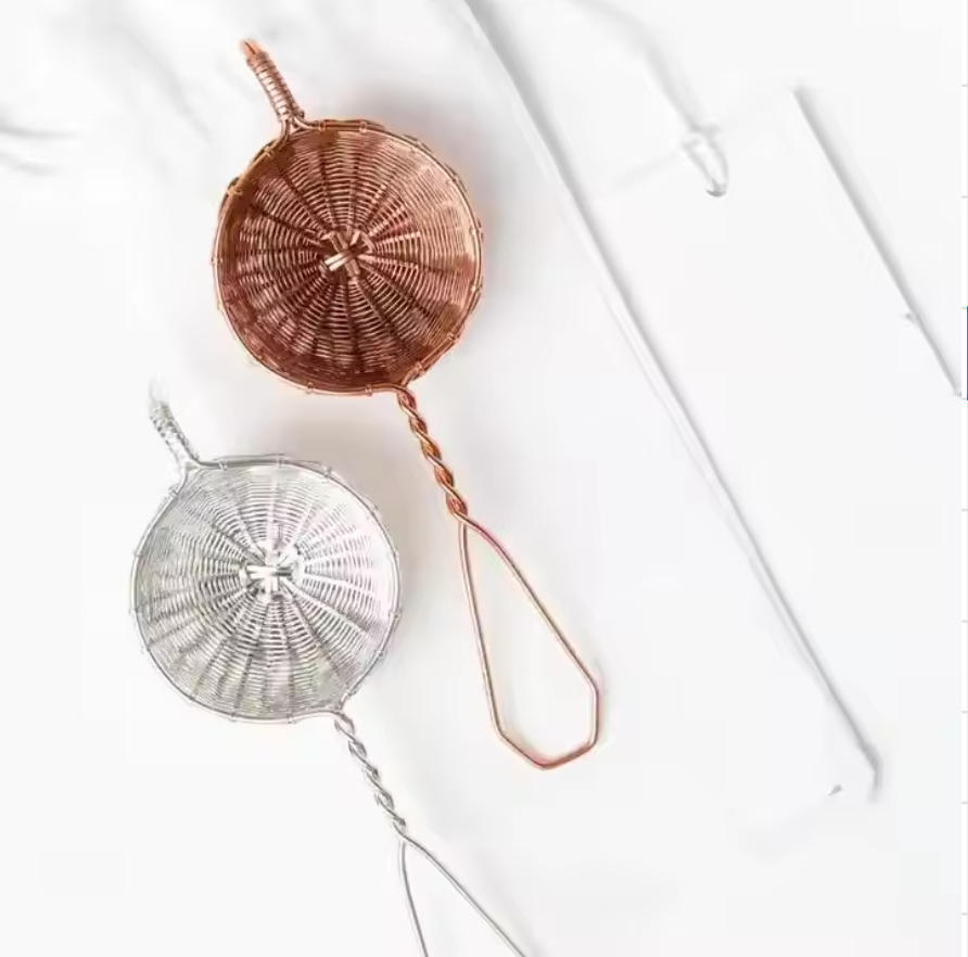 Two Fine Mesh Strainers, one silver and one copper, rest on a white surface. Each has a twisted handle; the copper strainer features an elongated loop handle. The background is clean and minimalistic.