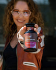 Zhena smiling in the background holding a violet glass apothecary jar of Fireside Chai herbal chai loose leaf tea.