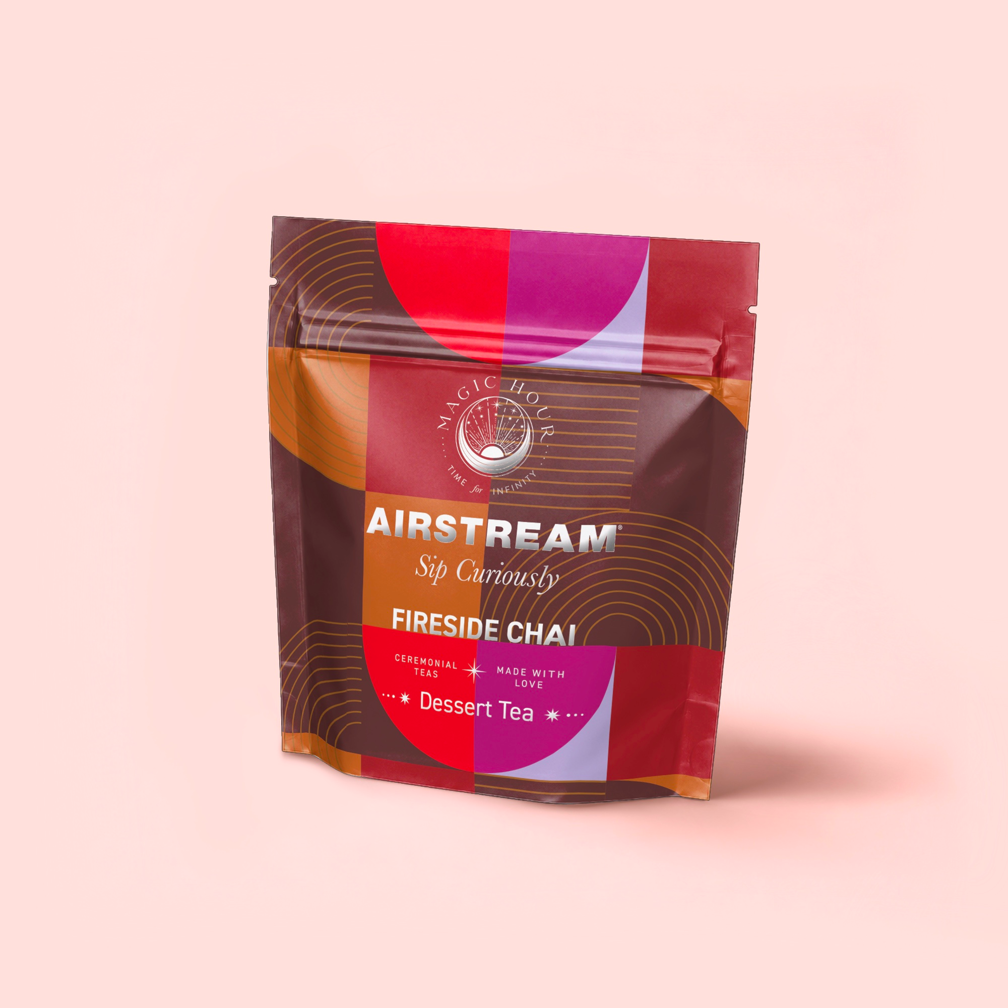 A colorful resealable pouch of Fireside Chai: Warming Rooibos Blend for Creating Connection—caffeine-free spiced herbal chai with Rooibos tea—in a red, orange, and purple geometric design on light pink. The packaging says "Sip Curiously.