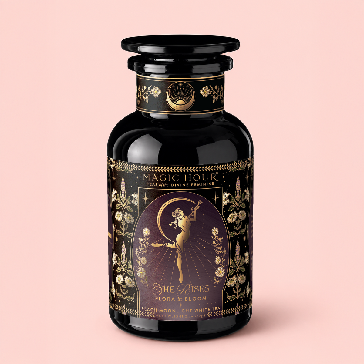 A black and gold tea jar labeled “Magic Hour,” adorned with floral patterns and an illustration of a dancing woman beneath a crescent moon, set against a pale pink background, captures the ethereal charm of Flora In Bloom: Peach Moonlight White Tea—an exceptional white tea renowned for its delicate elegance.