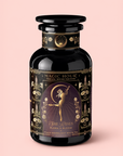 A black and gold tea jar labeled “Magic Hour,” adorned with floral patterns and an illustration of a dancing woman beneath a crescent moon, set against a pale pink background, captures the ethereal charm of Flora In Bloom: Peach Moonlight White Tea—an exceptional white tea renowned for its delicate elegance.