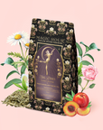 A package of Flora In Bloom: Peach Moonlight White Tea featuring a fairy-themed design is surrounded by daisies, roses, greenery, loose leaves of Moonlight White Tea (Yue Guang Bai), and a sliced peach, all arranged on a pale pink background.